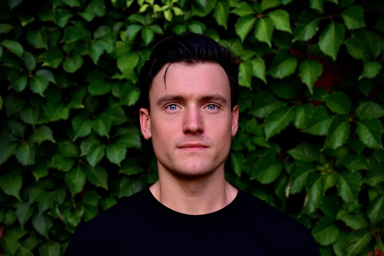 Perry Idyll in a black t-shirt against a wall of ivy